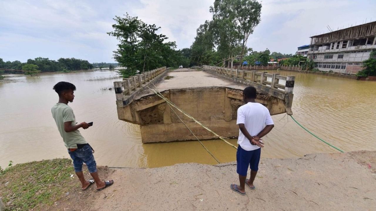People look at a damaged bridge washed out by the floods at Kampur in Nagaon District of Assam on June 27,2022. Credit: IANS Photo