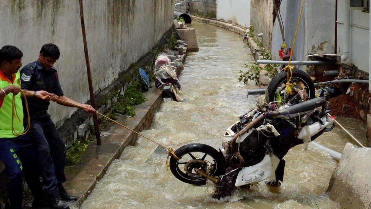 People trying to pull the two wheeler out which was washed away in the rain water due to heavy rainfall at KR Puram, in Bengaluru. Credit: IANS Photo