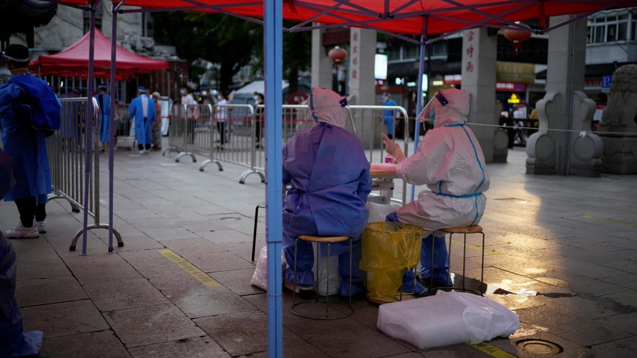 Medical workers in protective suits sit with ice blocks at a nucleic acid testing site amid a heatwave warning in Shanghai. Credit: Reuters photo