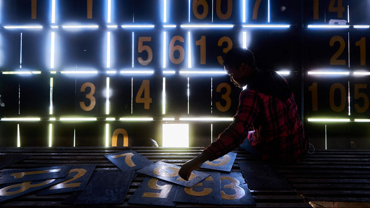 Admire Mupembe, a scoreboard operator, sorts out numbers from within the manual scoreboard during the cricket T20 World Cup Qualifier tournament at Queens Sports Club in Bulawayo, Zimbabwe on July 17, 2022. Credit: AFP Photo