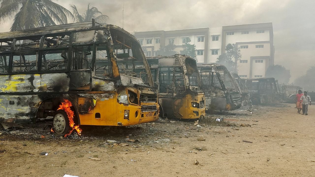 People walk past damaged school buses that were set on fire by a mob in Kallakurichi. Credit: Reuters photo