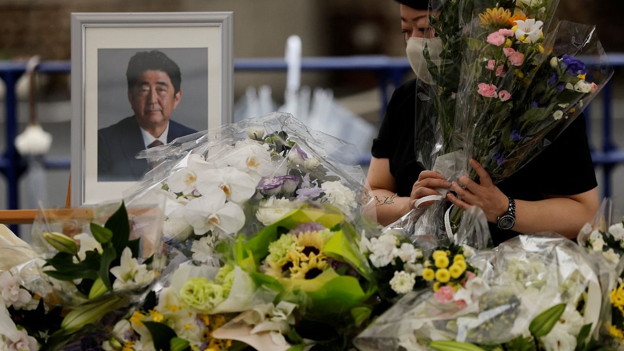 A mourner offers flowers next to a picture of late former Japanese Prime Minister Shinzo Abe. Credit: Reuters Photo