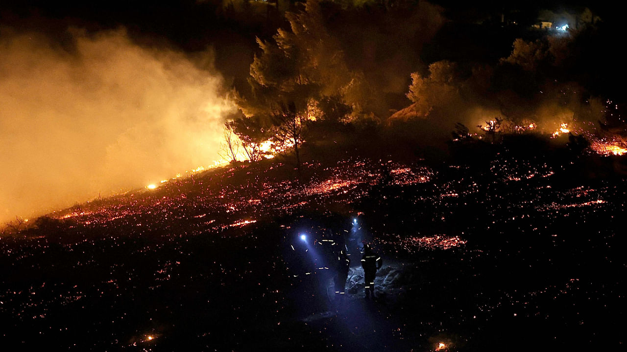 Firefighters use headlamps as they stand in ash as a wildfire rages in Anthousa, north of Athens, on July 19, 2022. Credit: AFP Photo