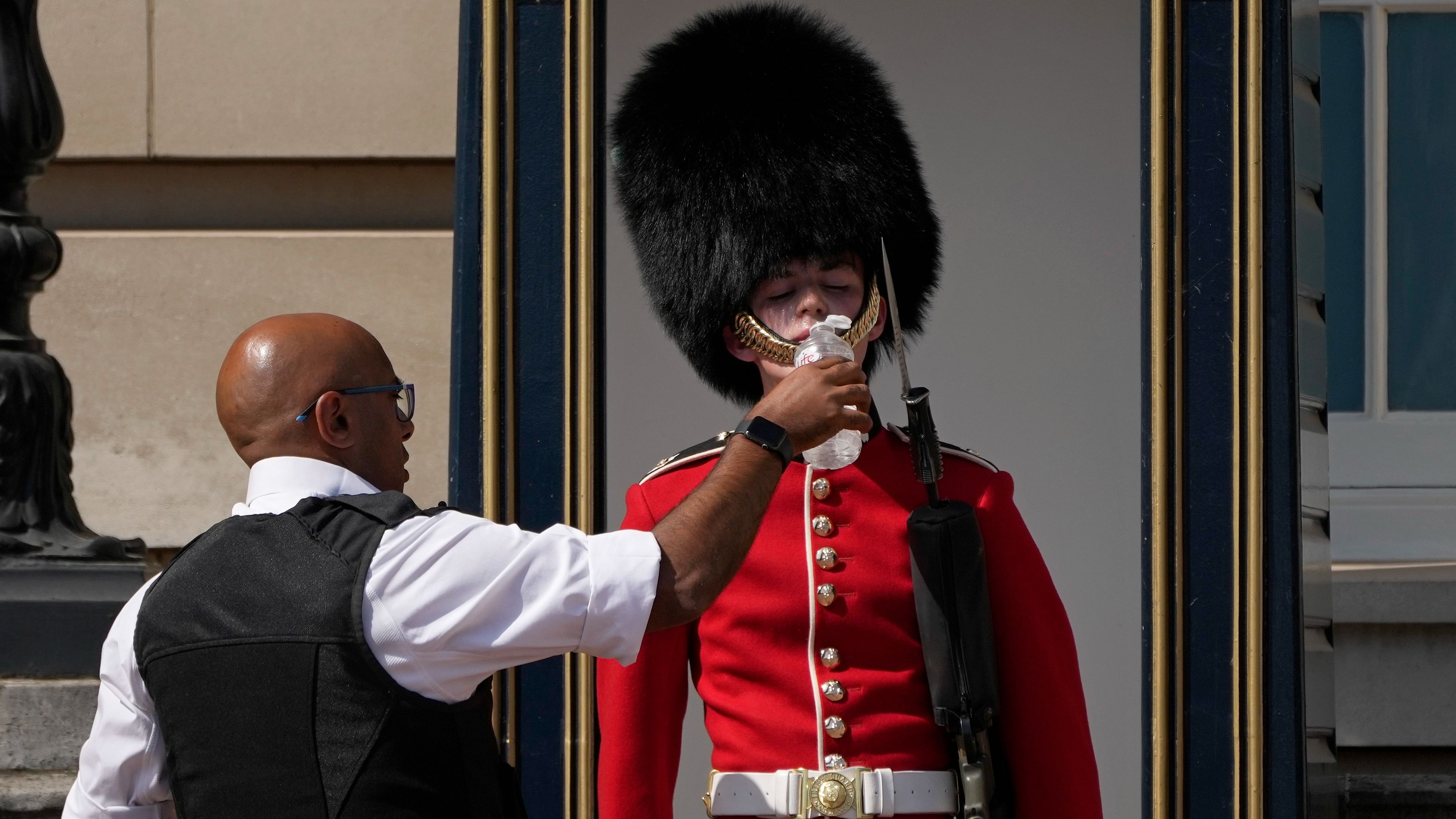 A police officer givers water to a British soldier wearing a traditional bearskin hat, on guard duty outside Buckingham Palace, during hot weather in London. Credit: AP/PTI File Photo