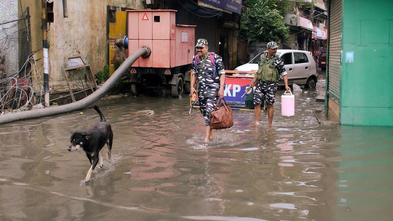 Security personnel wade through a flooded road following monsoon rains. Credit: PTI Photo