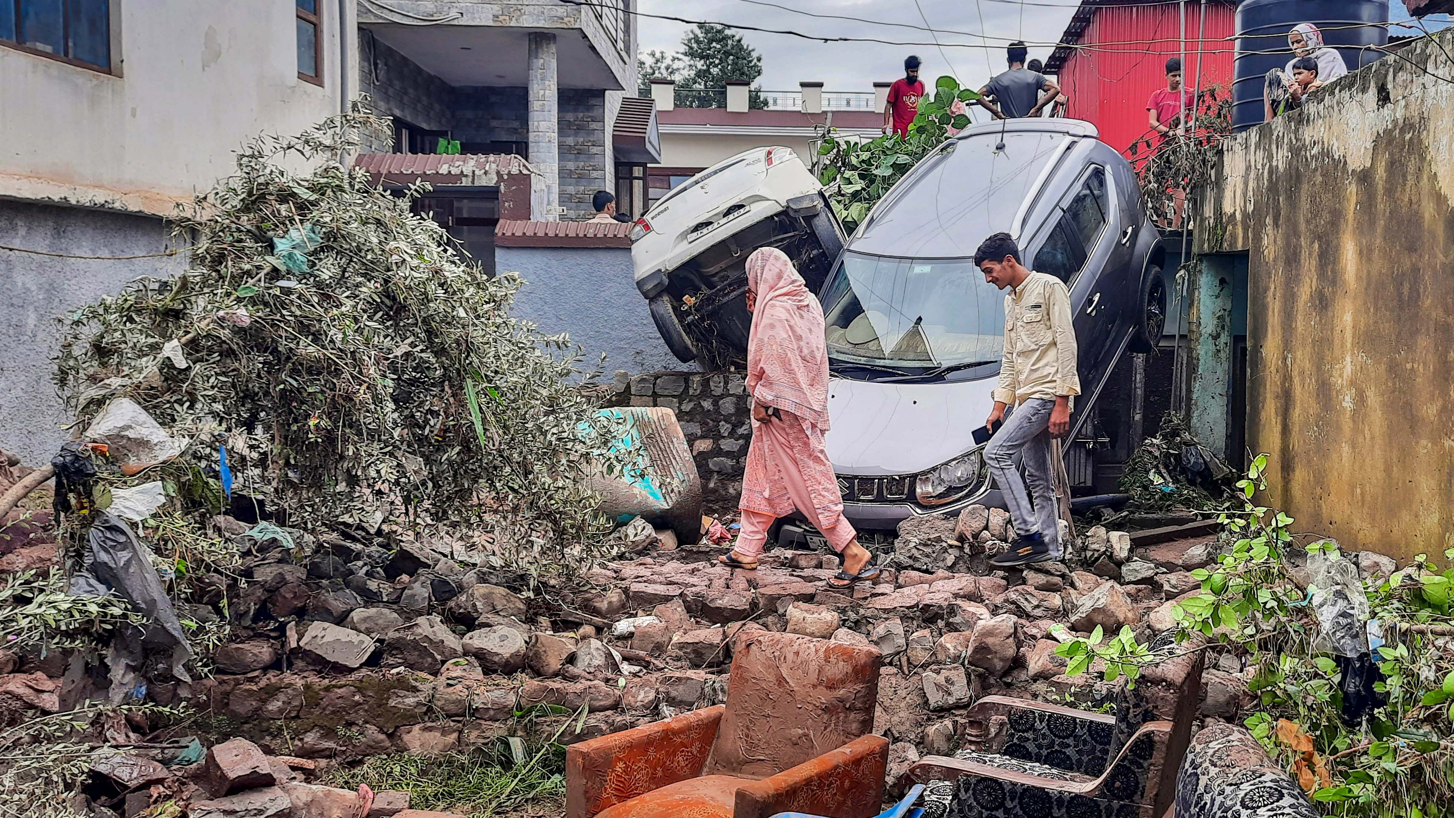  Locals walk amidst damaged vehicles and property after flash floods in the Surankote area of Poonch. Credit: PTI Photo 