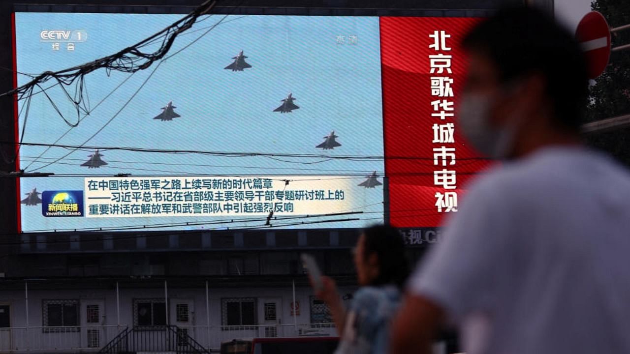 Pedestrians wait at an intersection near a screen showing footage of Chinese People's Liberation Army (PLA) aircraft during an evening news programme, in Beijing. Credit: Reuters Photo