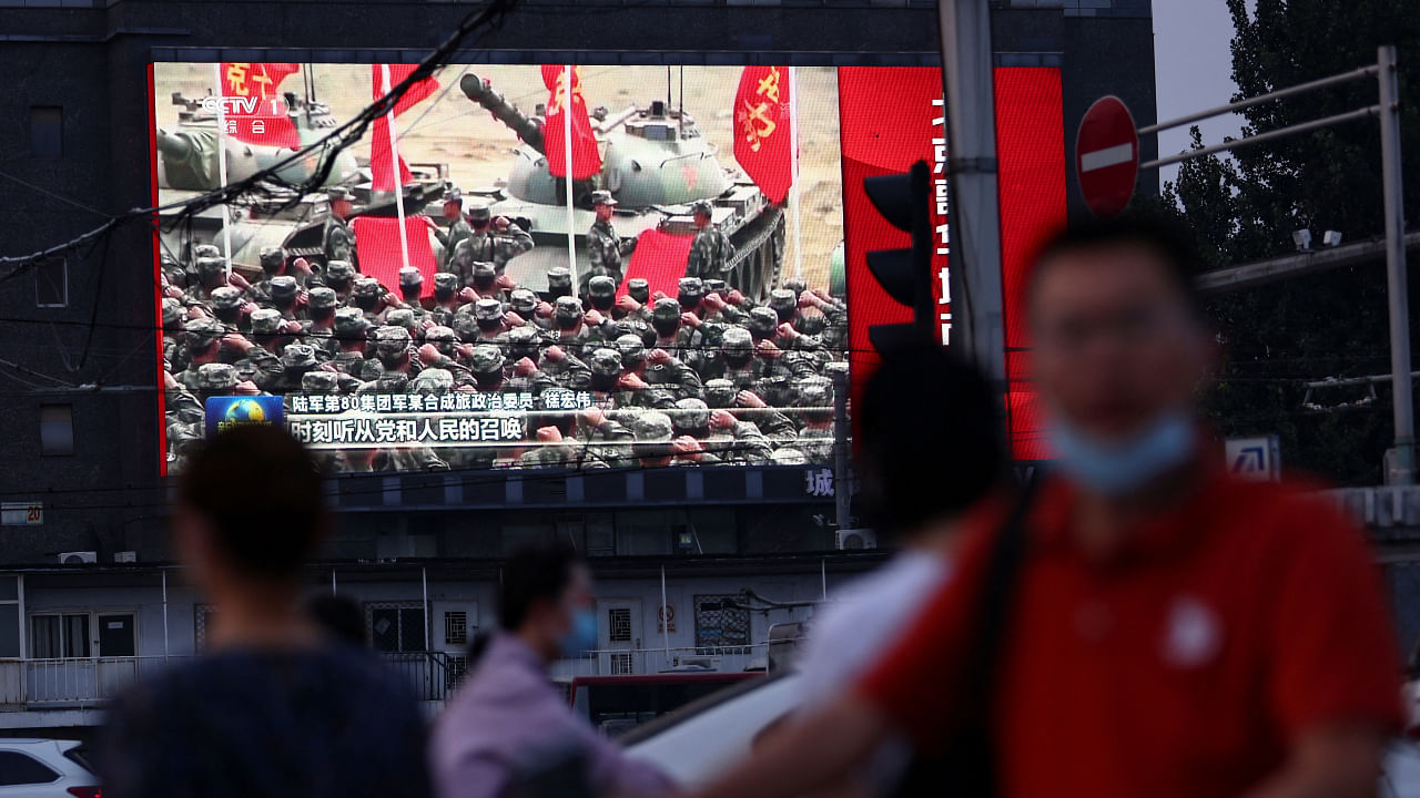 Pedestrians walk past a screen showing footage of Chinese People's Liberation Army (PLA) soldiers during an evening news programme, in Beijing, China August 2, 2022. Credit: Reuters Photo