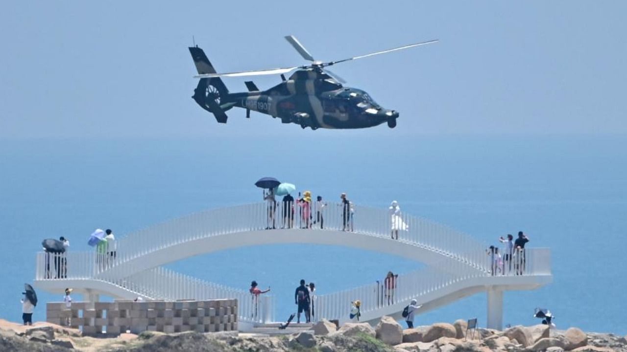 Tourists look on as a Chinese military helicopter flies past Pingtan island, one of mainland China's closest point from Taiwan, in Fujian province on August 4, 2022, ahead of massive military drills off Taiwan following US House Speaker Nancy Pelosi's visit to the self-ruled island. Credit: AFP Photo