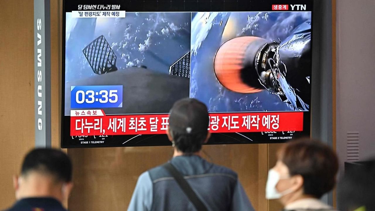 People watch a television screen showing a live footage of a SpaceX Falcon 9 rocket launching with South Korea's first lunar orbiter Danuri onboard from Cape Canaveral in Florida, at a railway station in Seoul on August 5, 2022. Credit: AFP Photo