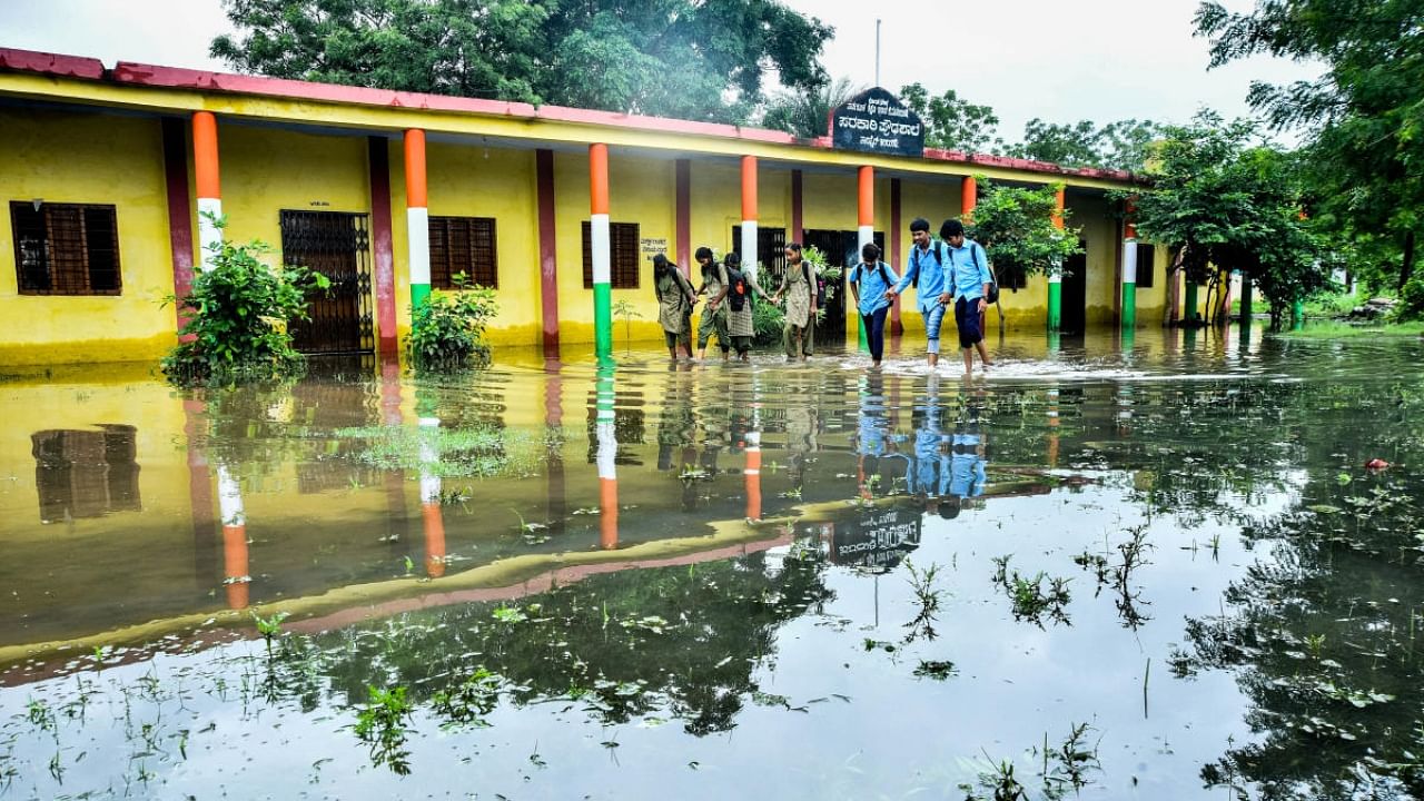 Students wade through the flooded school premises in Kalaburagi on Friday. Credit: DH Photo/Tajuddin Azad