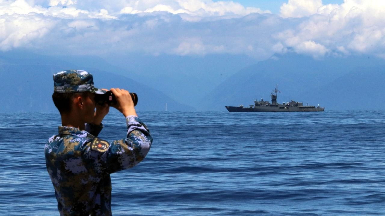 A People's Liberation Army member looks through binoculars during military exercises as Taiwan's frigate Lan Yang is seen at the rear. Credit: AFP Photo