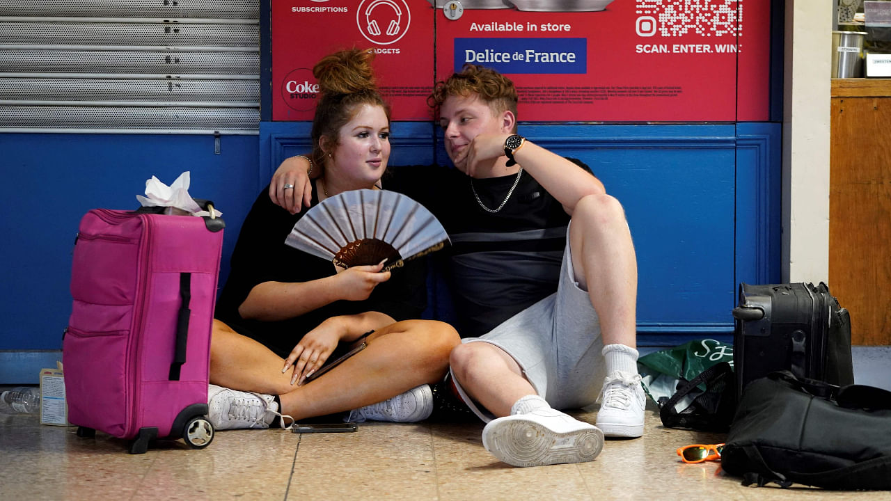 A rail passenger uses a fan to cool down as they sit with their belongings at Euston train station in central London, on July 19, 2022. Credit: AFP File Photo