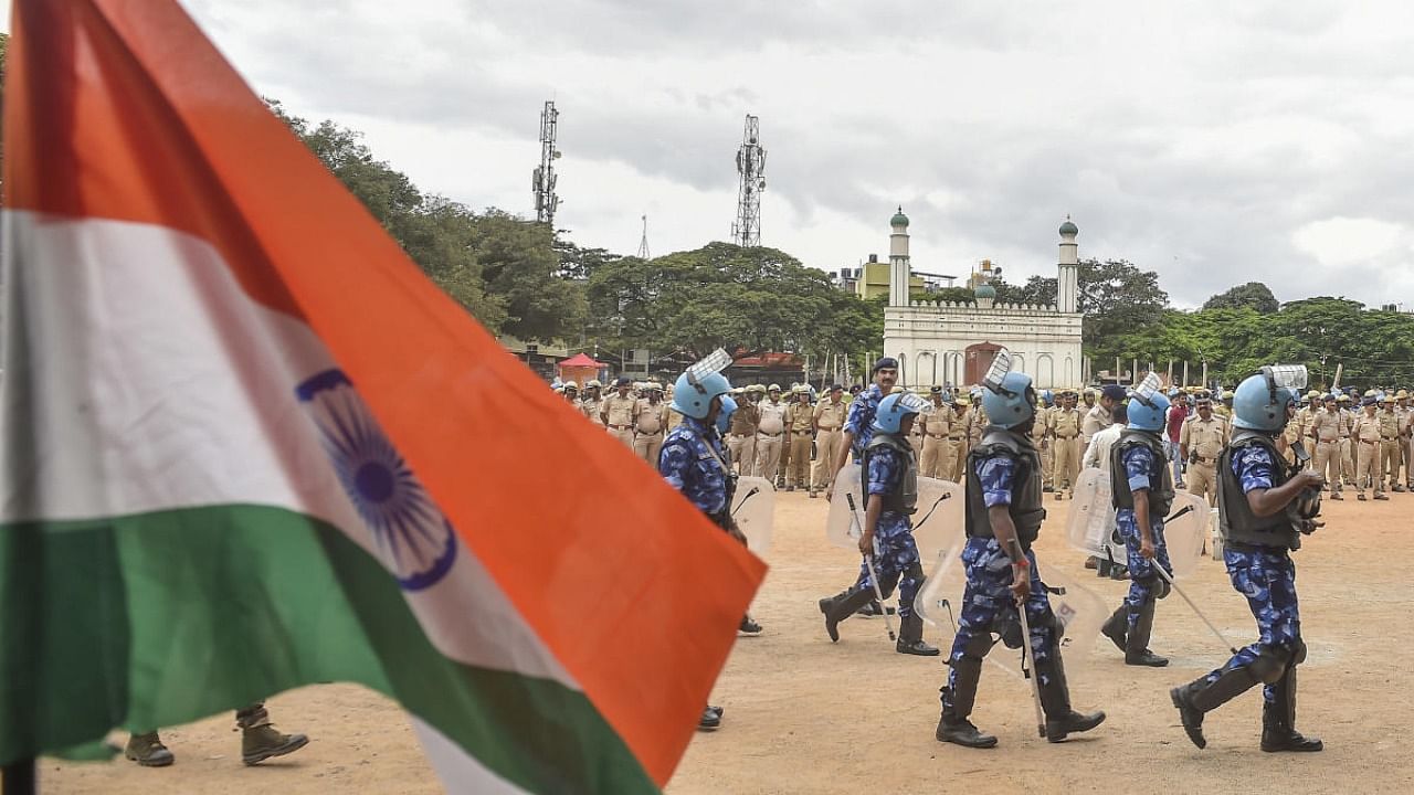 The national flag is seen in the foreground as Rapid Action force (RAF) and Karnataka police personnel patrol on the disputed Idgah Maidan. Credit: PTI Photo