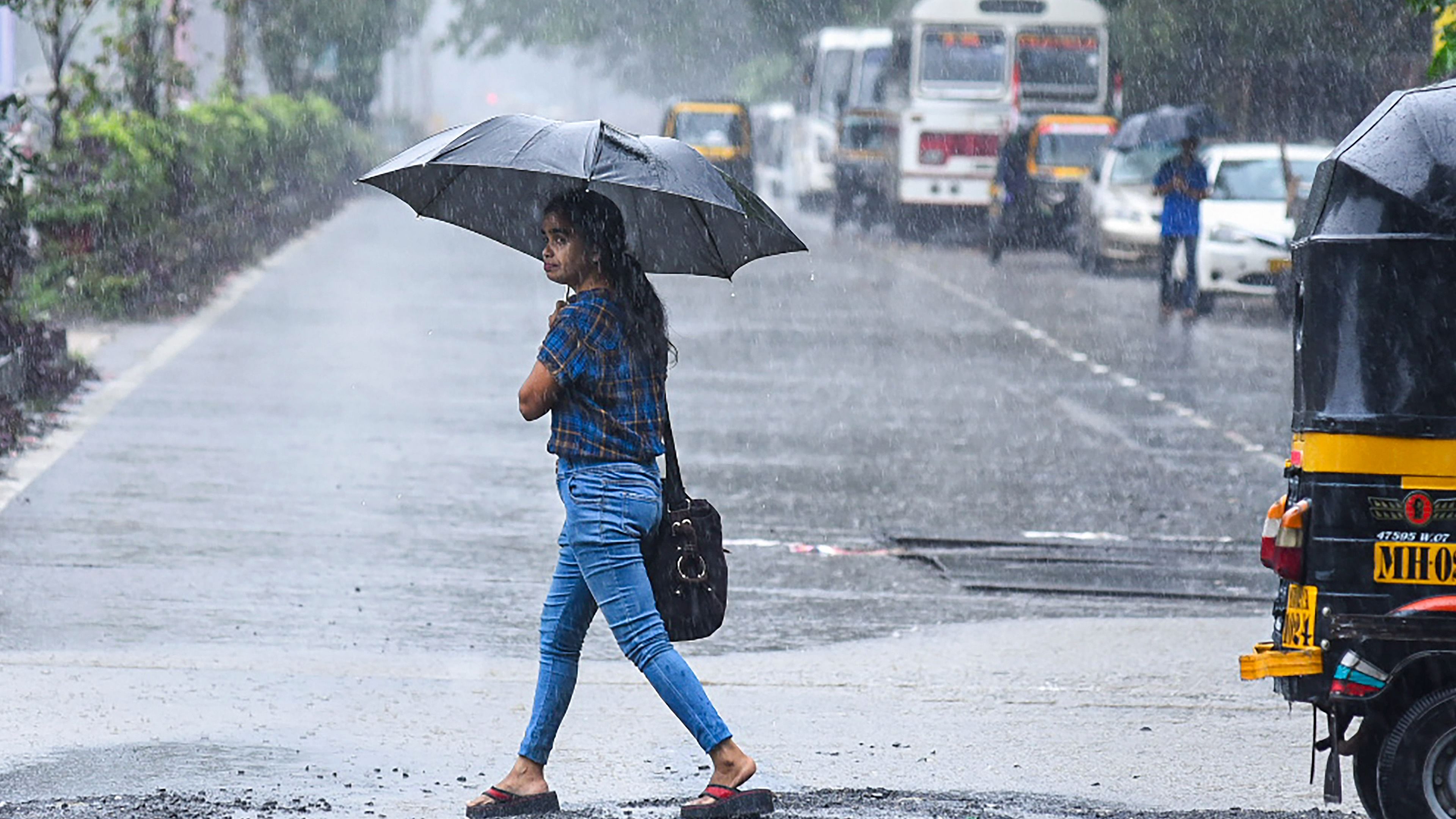 A woman holding an umbrella crosses a road amid monsoon rains, in Mumbai. Credit: PTI Photo