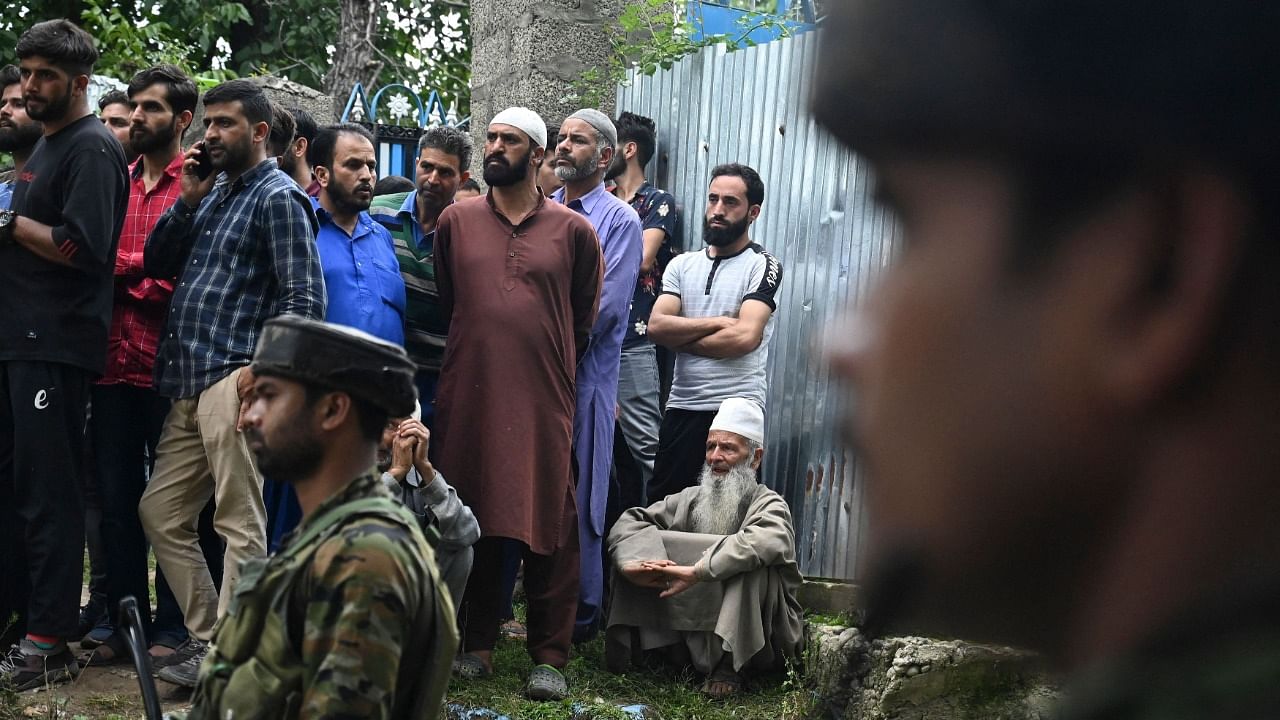 Security forces stand guard as neighbours gather outside the house of Sunil Kumar, who belonged to the Kashmiri Pandit community, after militants shot him dead at an apple orchard in Chotipora area of Shopian. Credit: AFP Photo