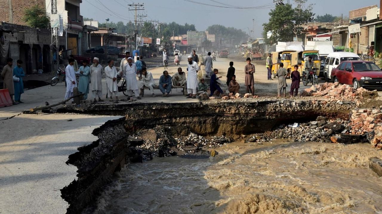 Residents gather beside a road damaged by flood waters following heavy monsoon rains in Charsadda district of Khyber Pakhtunkhwa. Credit: AFP Photo