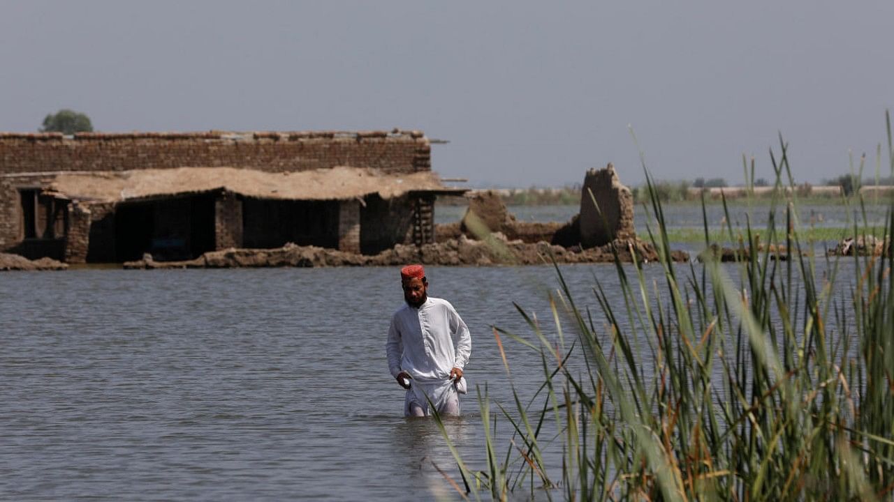 A flood victim man wades through flood water with a damaged house in the background, following rains and floods during the monsoon season in Gari Yasin, Pakistan. Credit: Reuters Photo