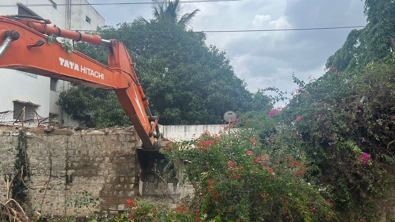 BBMP deploys earth mover to raze an illegally built compound wall in Mahadevapura. Credit: DH Photo