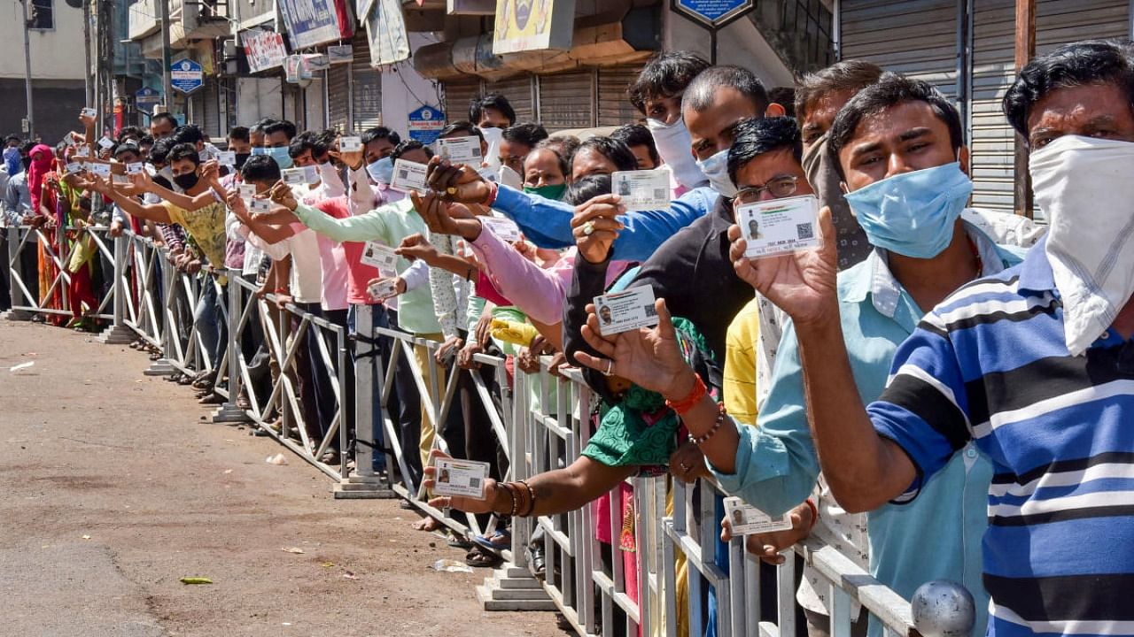People hold their Aadhaar Card as they stand in a queue to collect free food grains from a government controlled shop. Credit: PTI file photo