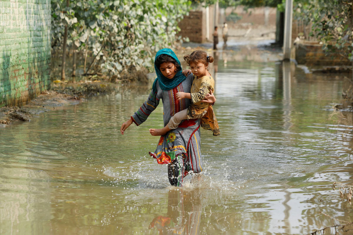A girl carries her sibling as she walks through stranded flood water, following rains and floods during the monsoon season in Nowshera, Pakistan. Credit: REUTERS
