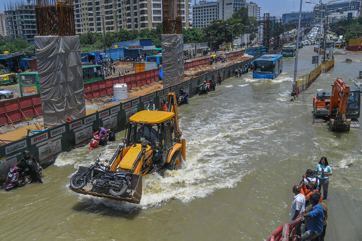 An excavator transports a two-wheeler along an inundated stretch of the Outer Ring Road in Bengaluru on Monday. Credit: DH Photo/S K Dinesh