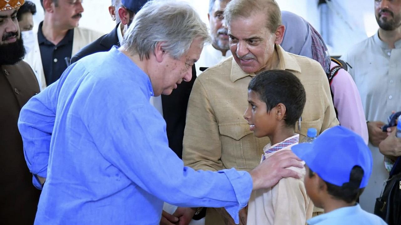 Prime Minister Shahbaz Sharif, center right, and UN Secretary-General Antonio Guterres, left, interact with children at a school set up at a flood relief camp in Jaffarabad, Pakistan. Credit: AP Photo