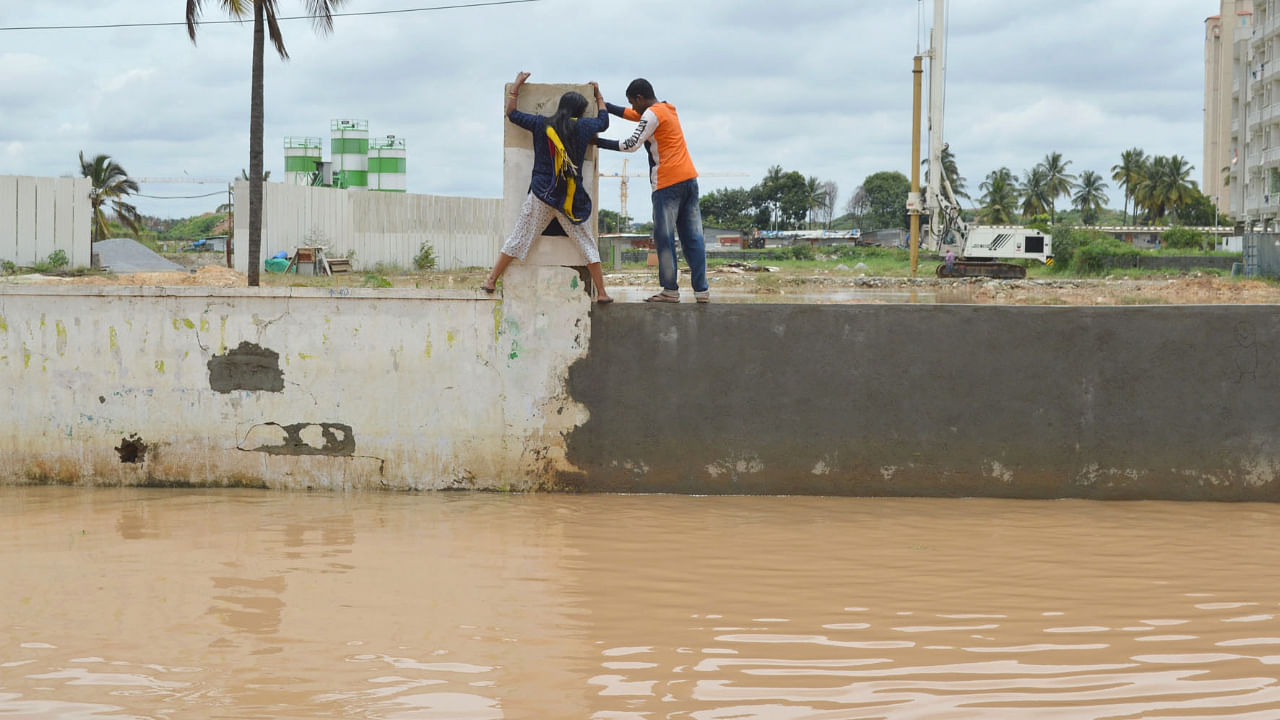 People seen climbing walls to avoid the submerged roads at Bellandur, following heavy rainfall in the city. Credit: IANS Photo