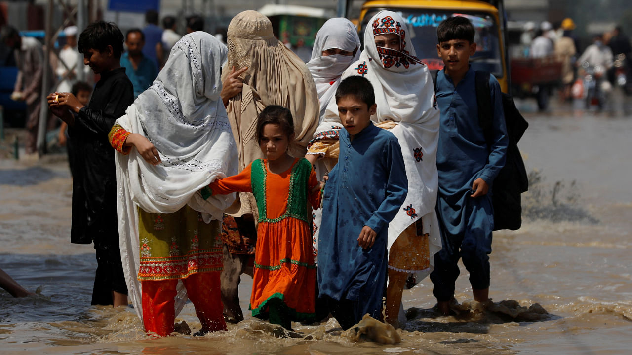 A family walk along a flooded street, following rains and floods during the monsoon season in Nowshera, Pakistan August 30, 2022. Credit: Reuters Photo