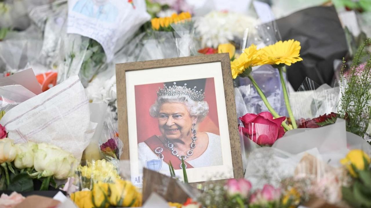 A portrait of Britain's Queen Elizabeth II is seen amongst flowers put down by well-wishers outside of Buckingham Palace in London on September 10, 2022, two days after she died at the age of 96. Credit: AFP Photo