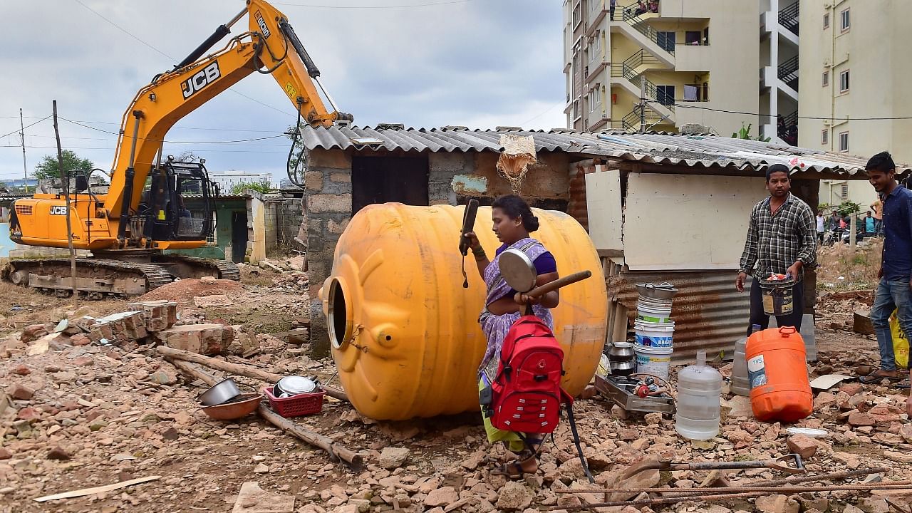 Migrants shift with their belongings as a Bruhat Bengaluru Mahanagara Palike (BBMP) bulldozer demolishes an illegal structure built on storm-water drain in Munnekolala area, which was recently flooded due to heavy monsoon rains, in Bengaluru. Credit: PTI Photo