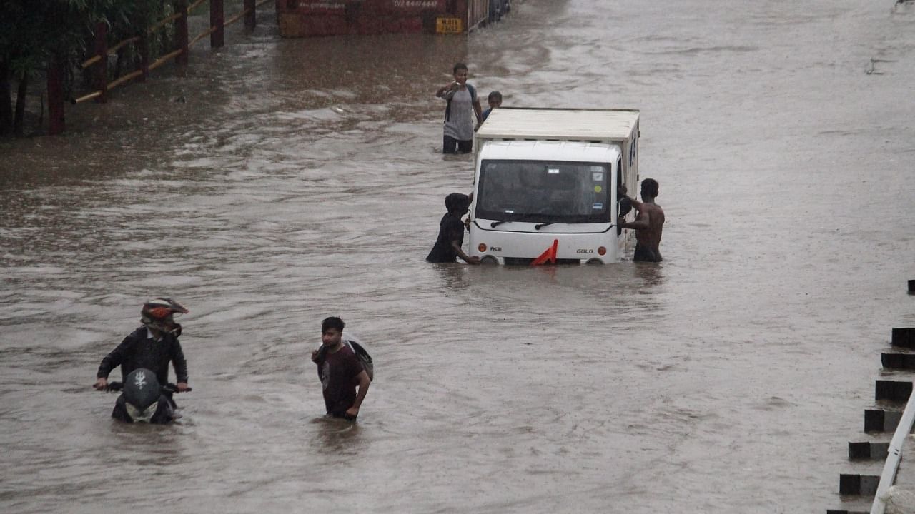 Commuters push their vehicle down the waterlogged Delhi-Gurugram Expressway service road after rainfall. Credit: PTI Photo