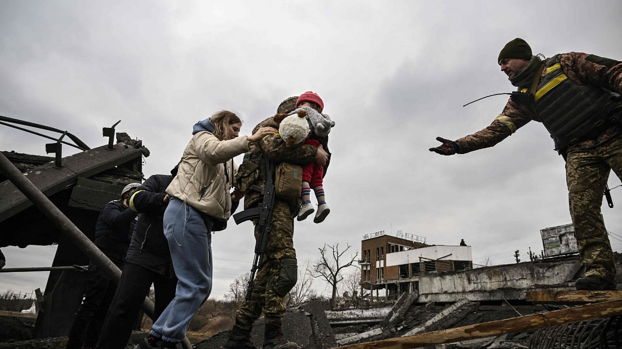 A Ukrainian serviceman carries a child while assisting people to cross a destroyed bridge as they evacuate the city of Irpin, northwest of Kyiv. Credit: AP Photo