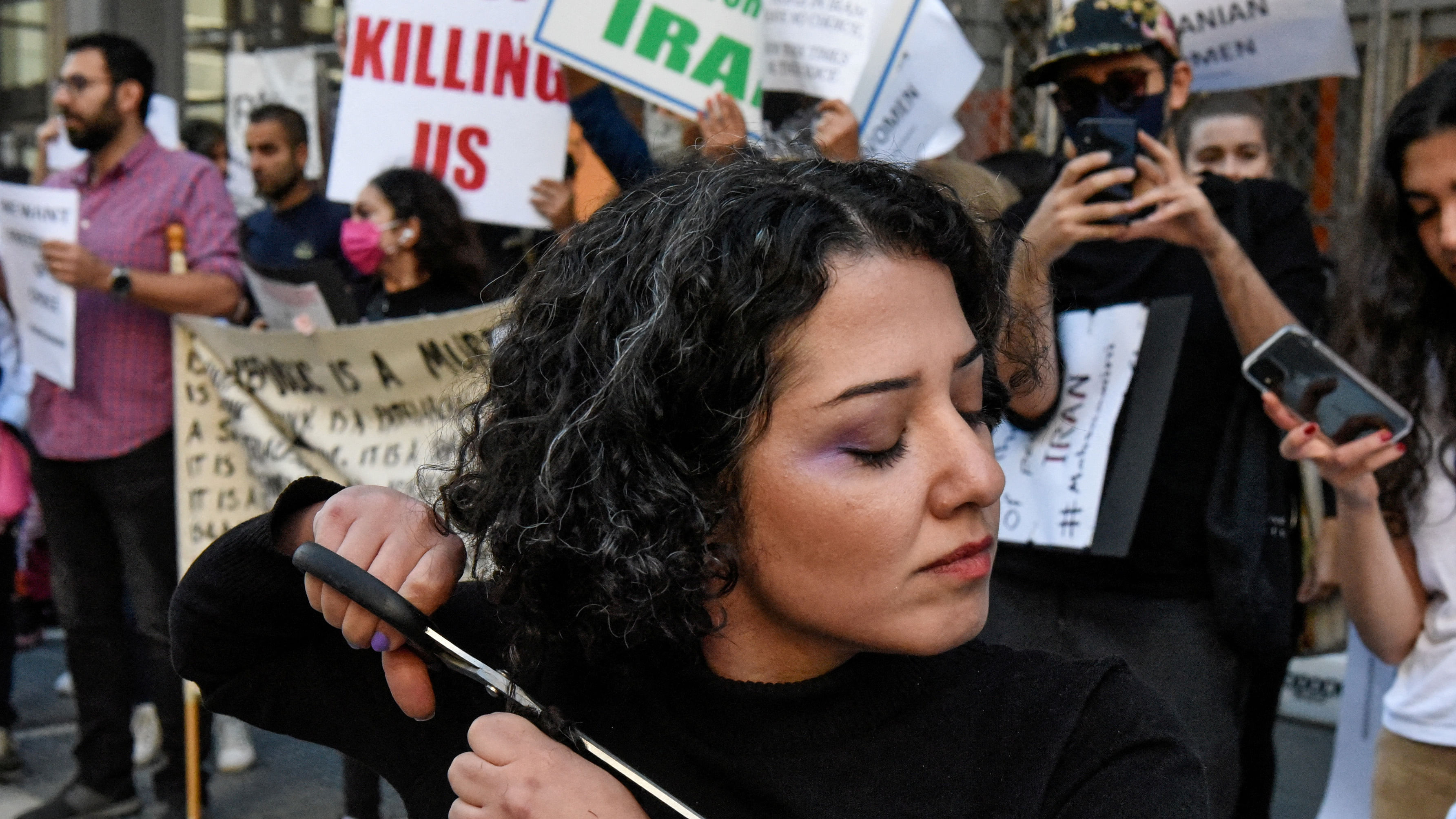 A woman cuts her hair during a protest against the Islamic regime of Iran and the death of Mahsa Amini in New York City. Credit: Reuters Photo