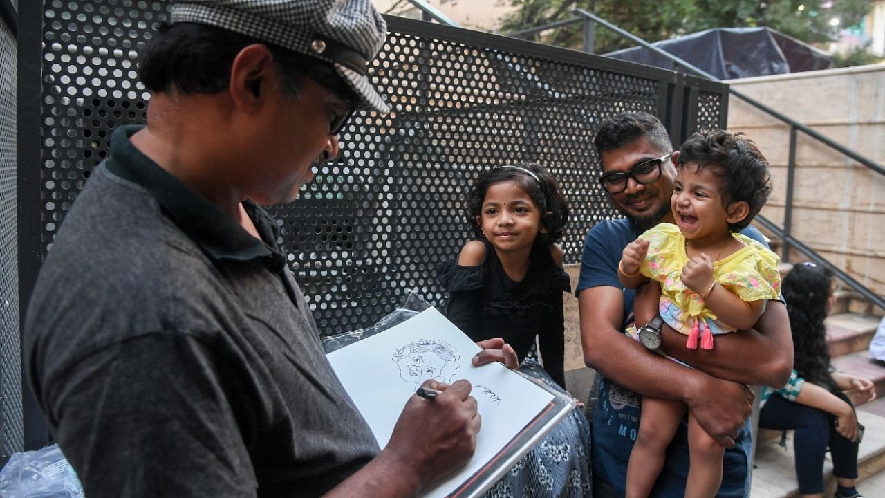 The journalist draws the caricature of a kid as she looks on happily, on Church Street. Credit: DH Photo/ B H Shivakumar