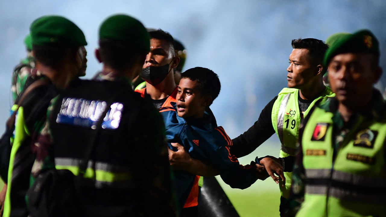 This picture taken on October 1, 2022 shows a boy (C) being carried as members of the Indonesian army secure the pitch after a football match between Arema FC and Persebaya Surabaya at Kanjuruhan stadium in Malang, East Java. Credit: AFP Photo