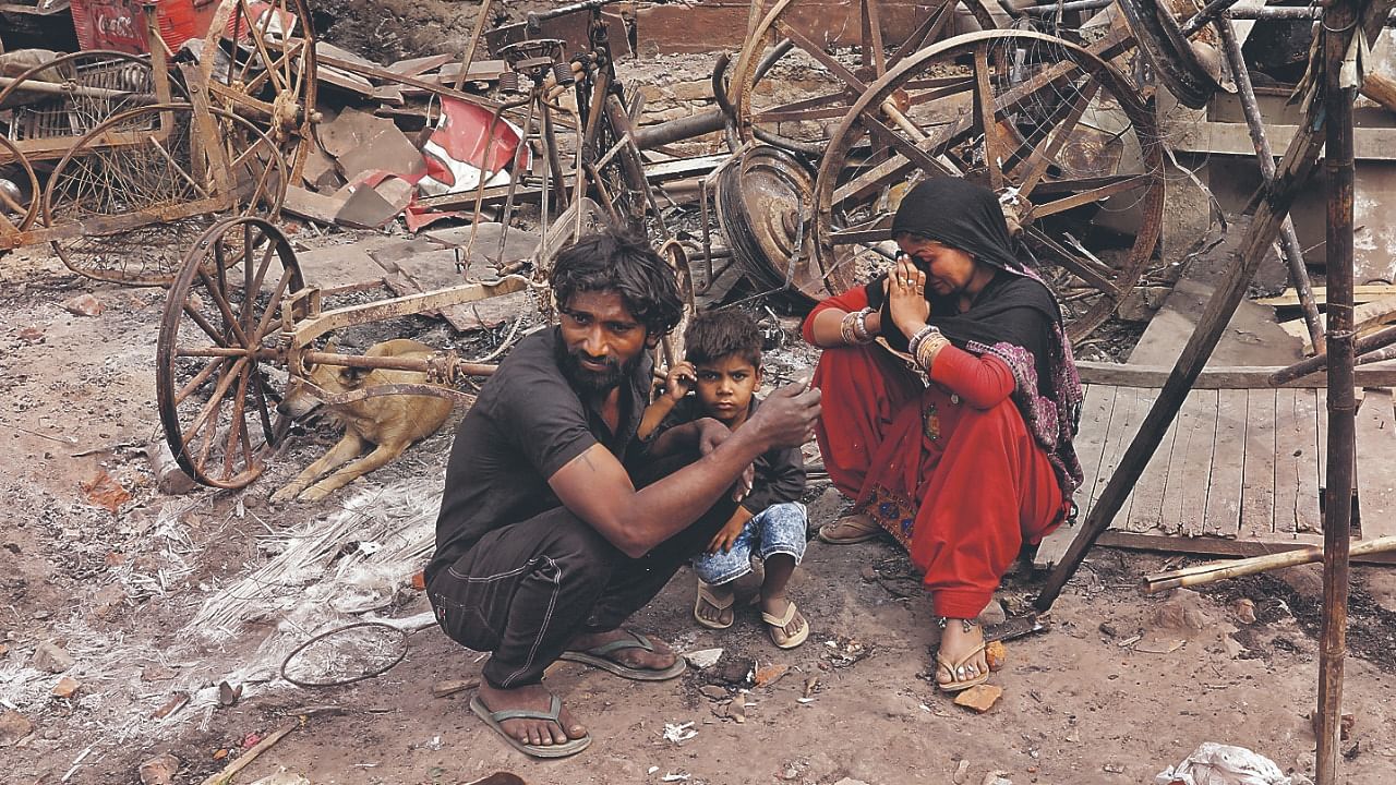 A woman sitting with her husband and their child reacts next to damaged property after their house was burnt by a mob on Tuesday in a riot affected area in New Delhi. Credit: Reuters Photo