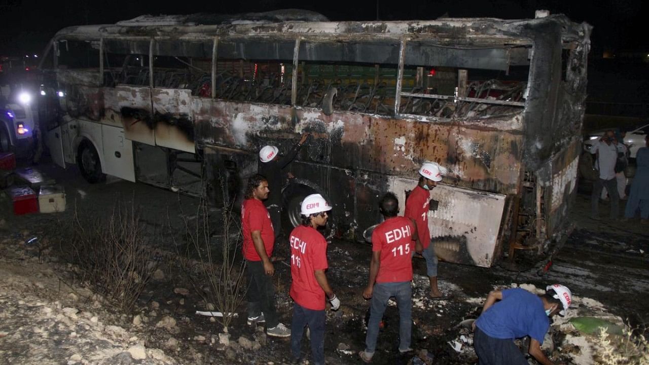 Volunteers gather beside a charred bus on a highway in Nooriabad, Pakistan. Credit: AP Photo