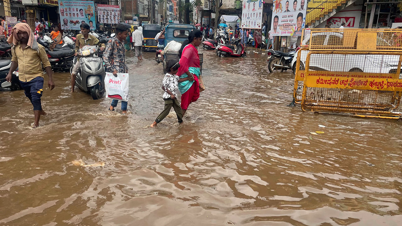 Commuters wade through a waterlogged street following rains, in Hubballi. Credit: PTI Photo