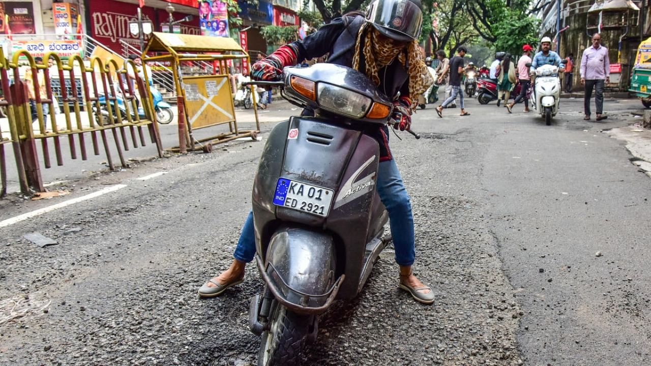 A woman bumps into a crater-like pothole on BVK Iyengar Road. Credit: DH Photo