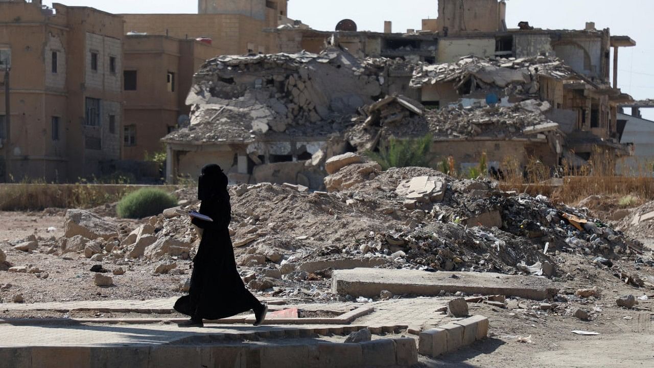 A woman walks past damaged buildings in Syria. Credit: Reuters File Photo