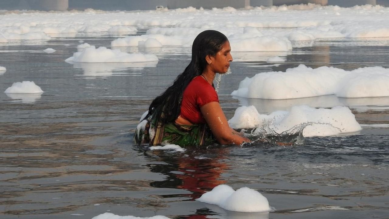 Devotees seen taking a dip in the Yamuna river as white, toxic foam covered the river in New Delhi. Credit: IANS Photo
