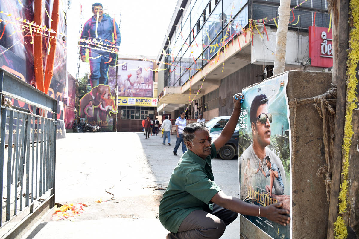 A worker pasting a poster of Punithrajkumar movie “Gandhada gudi” at the theatre in Bengaluru on Thursday. Credit: DH Photo/B K Janardhan