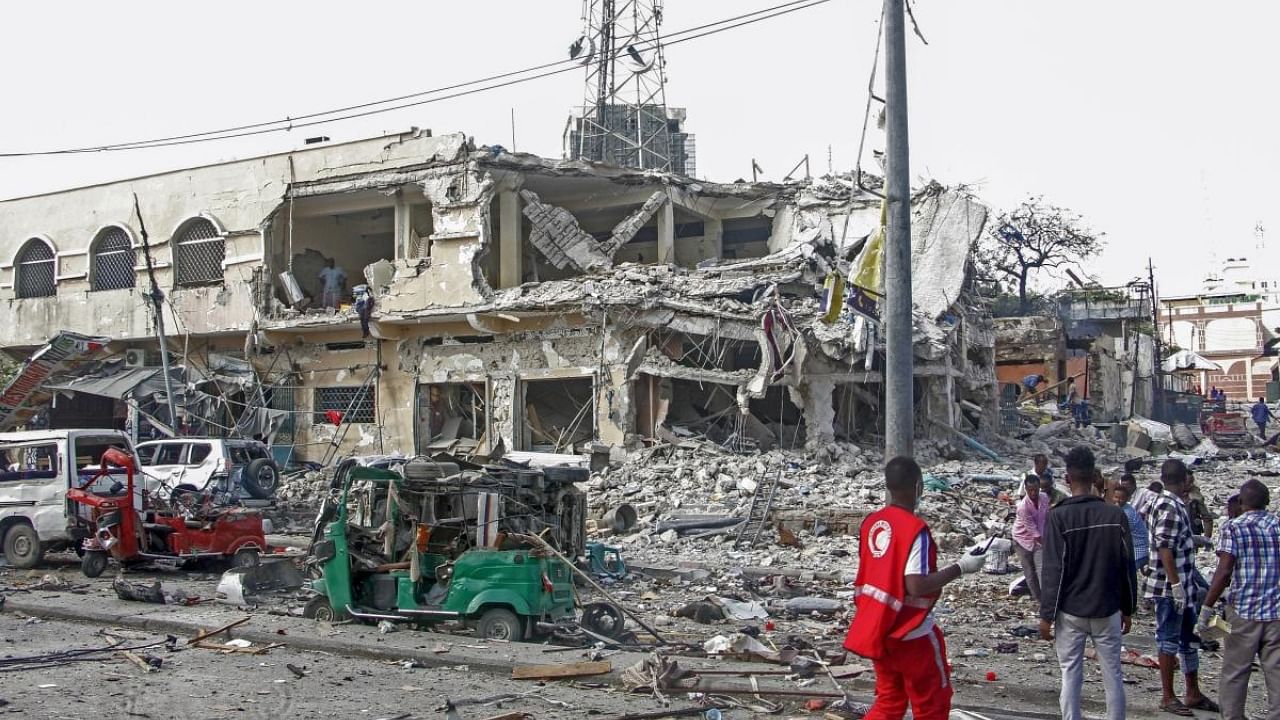 People observe a destroyed building and vehicles at the scene of a two car bombs attack in Mogadishu. Credit: AP/PTI Photo