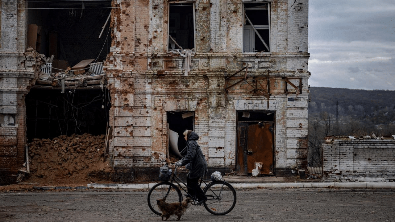 A woman rides a bicycle past a damaged building in the town of Kupiansk. Credit: AFP Photo