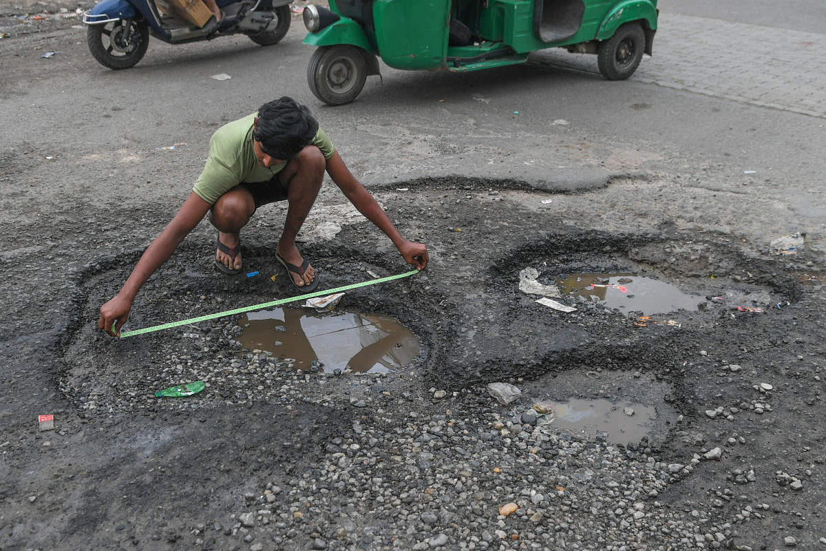 A boy measures a pothole on Nawab Hyder Ali Road near Kalasipalyam bus stand in Bengaluru on November 2. Credit: DH Photo