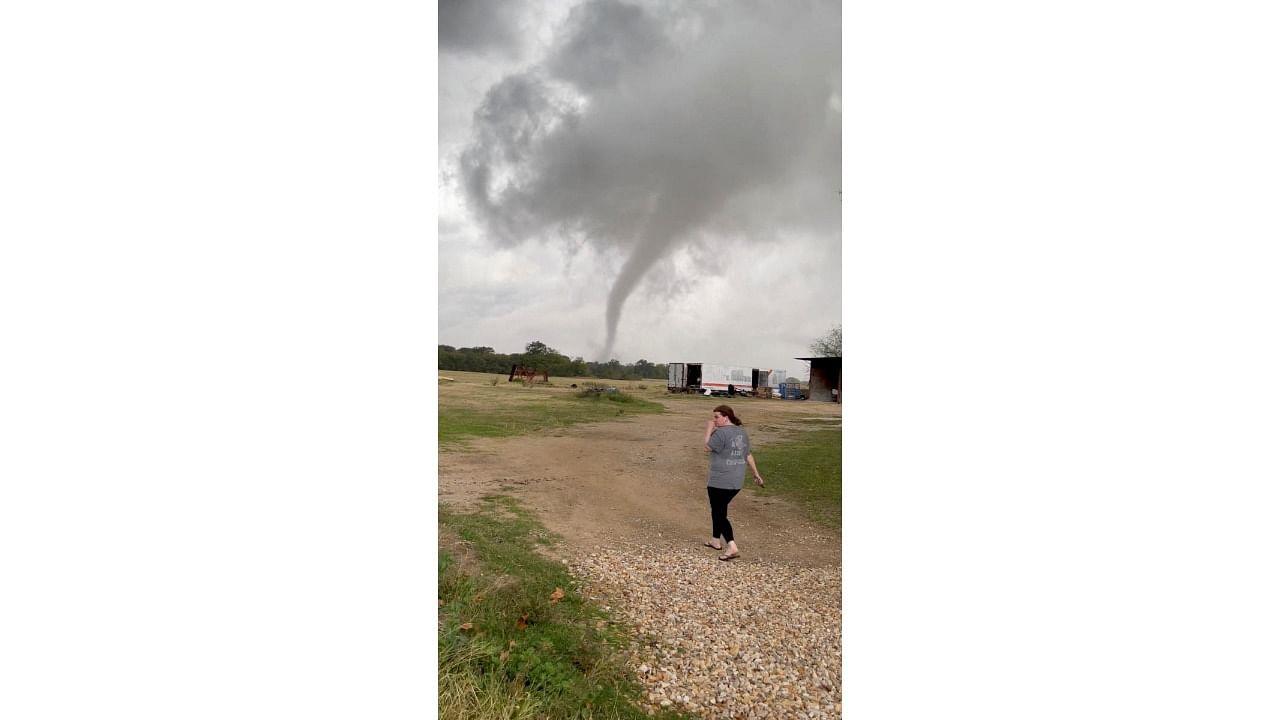 A woman walks in a farm as the funnel cloud of a tornado is seen in the background, in Greenview, Texas. Credit: Reuters photo/Twitter/@RCF_2008