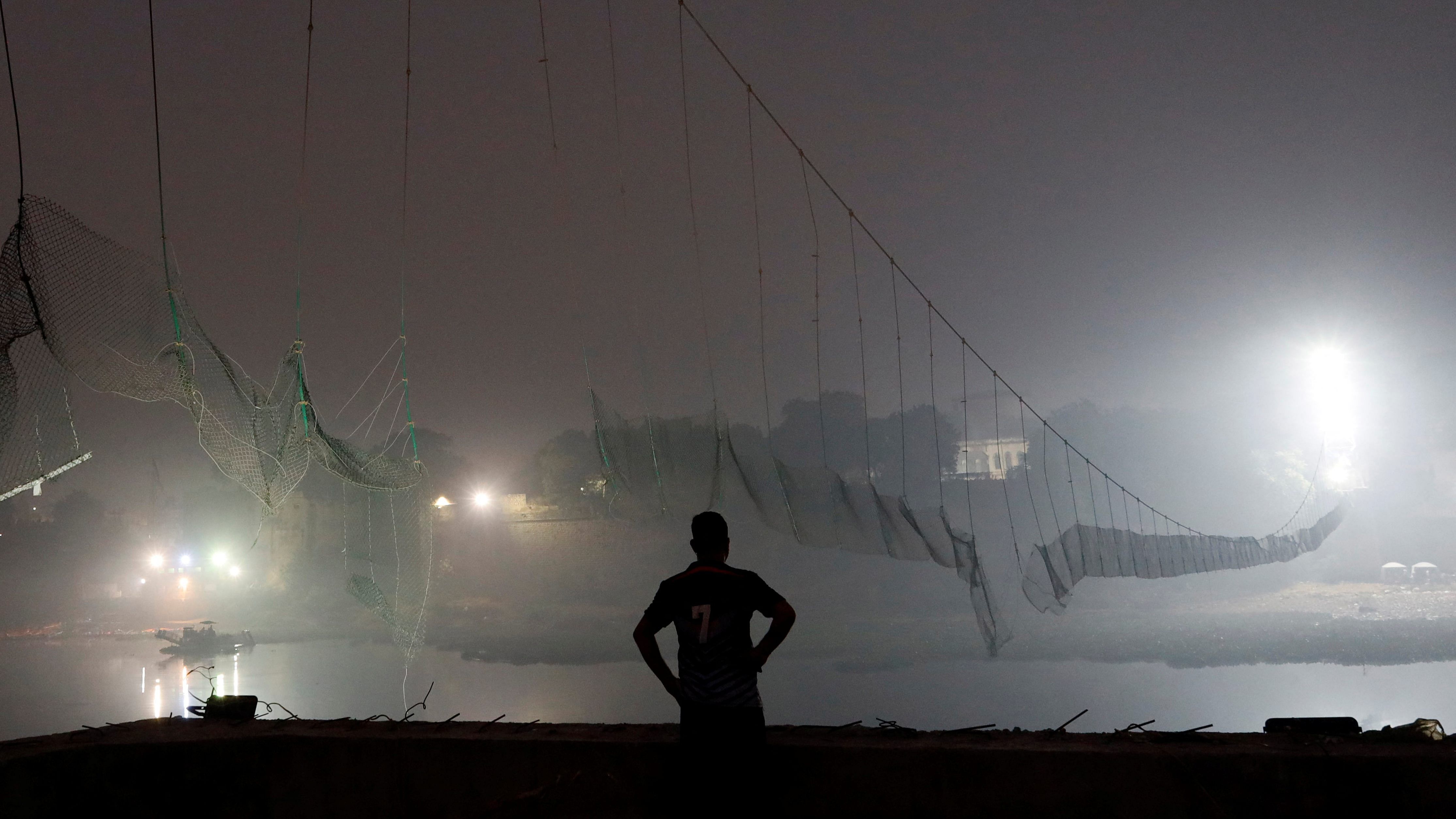 A security personnel stands near a damaged suspension bridge after it collapsed in Morbi. Credit: Reuters Photo