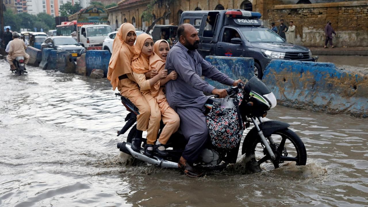 A man and students ride on a motorcycle on a flooded road, following rains during the monsoon season in Karachi. Credit: Reuters file photo