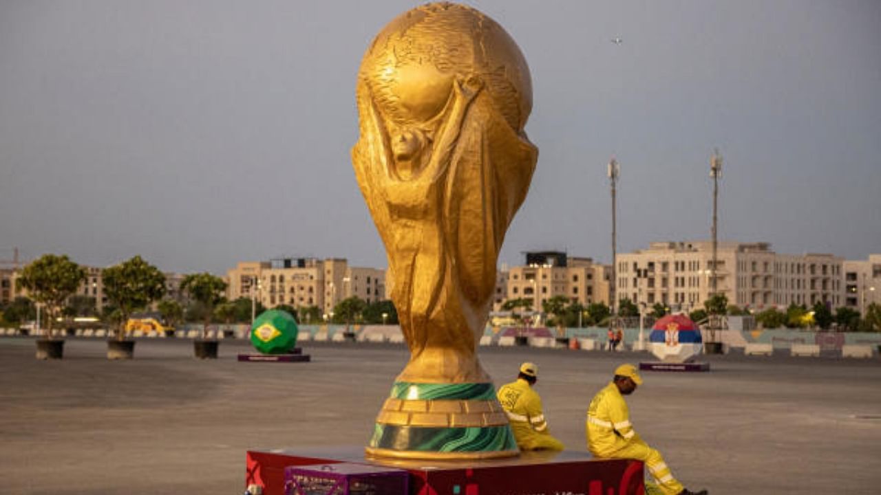 Workers sit beside a replica of the World Cup outside Lusail Stadium. Credit: Reuters Photo